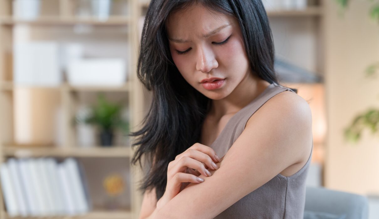 Woman examining dry skin in a bathroom affected by hard water while using a sensitive skin cleanser, active skincare, and the best niacinamide serum.