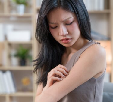 Woman examining dry skin in a bathroom affected by hard water while using a sensitive skin cleanser, active skincare, and the best niacinamide serum.