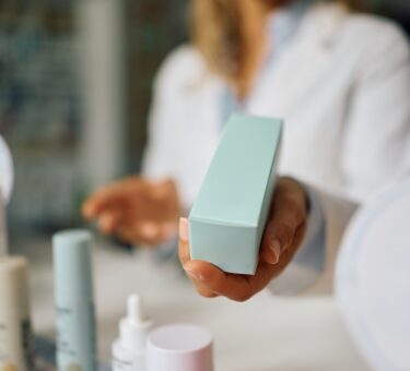 Woman comparing active skincare products, retinal cream, and acne prone skincare products while deciding whether expensive skincare is worth the price.
