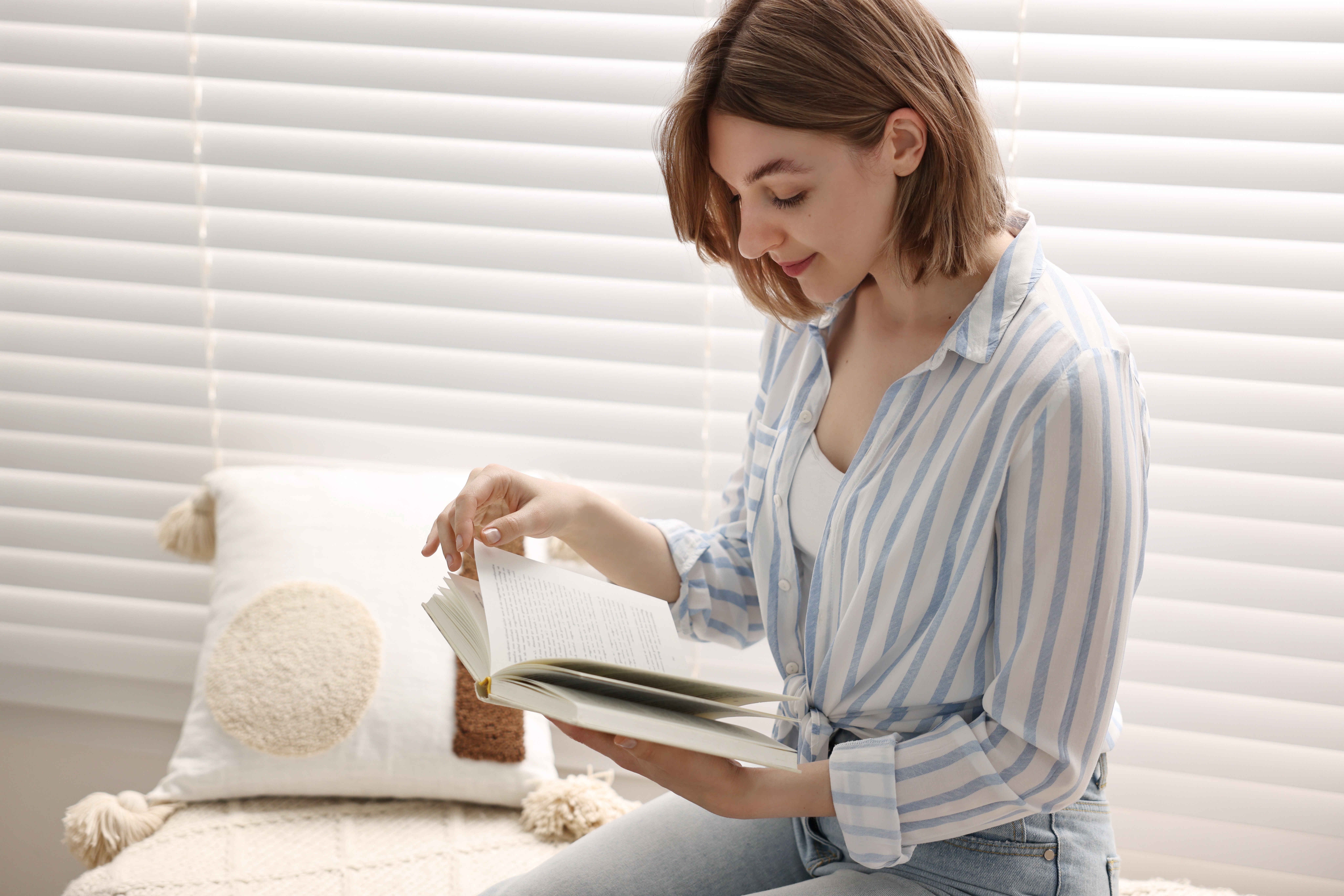 Relaxed woman reading in front of motorised timber shutters in a well lit room.